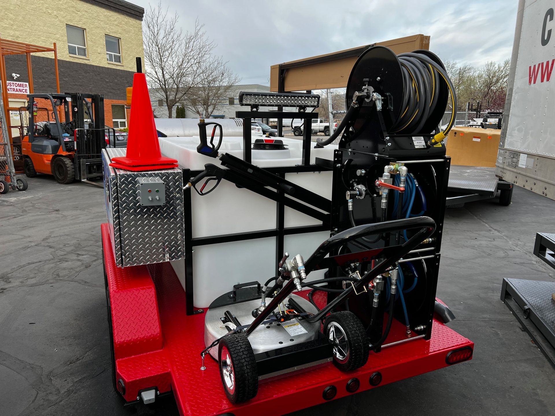 A red trailer with a hose reel attached to it is parked in a parking lot.865 Power Wash equipment