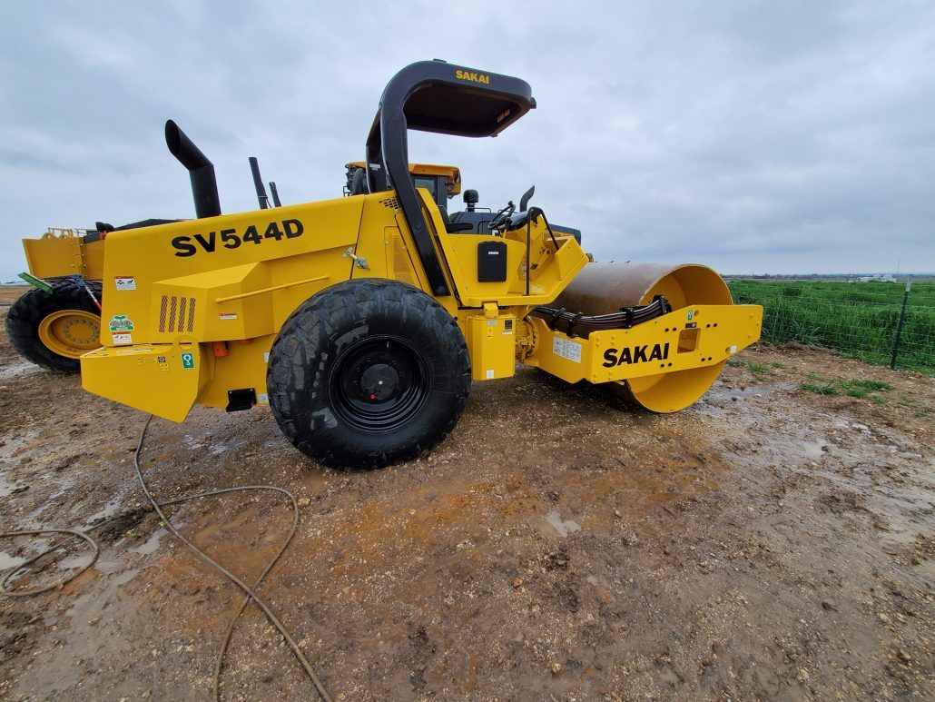 A yellow road roller is sitting on top of a dirt hill.
