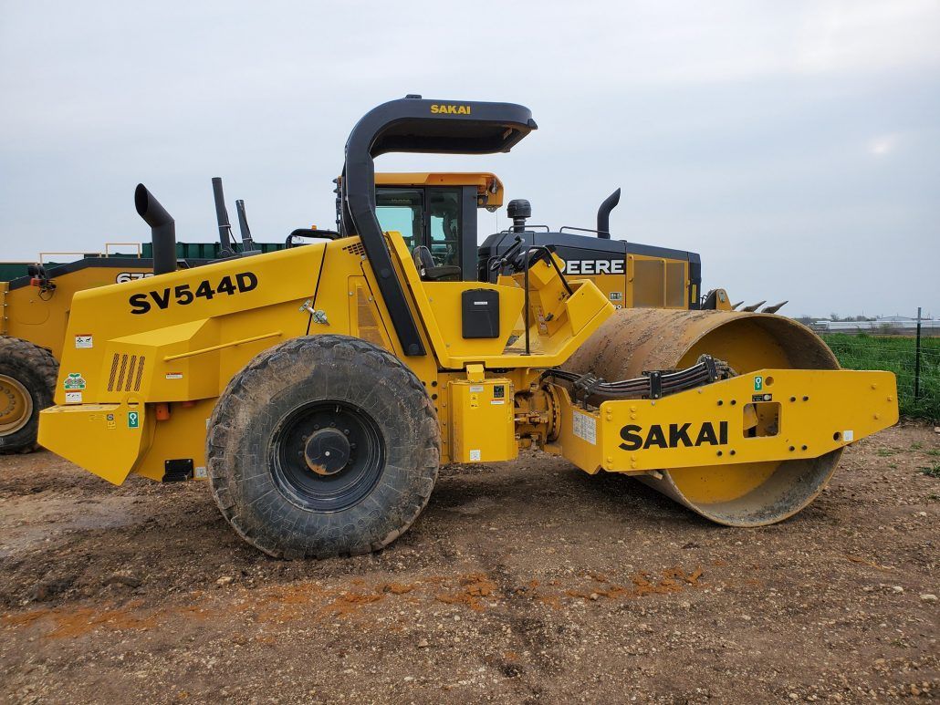 A yellow sakai vibratory roller is parked in a field.