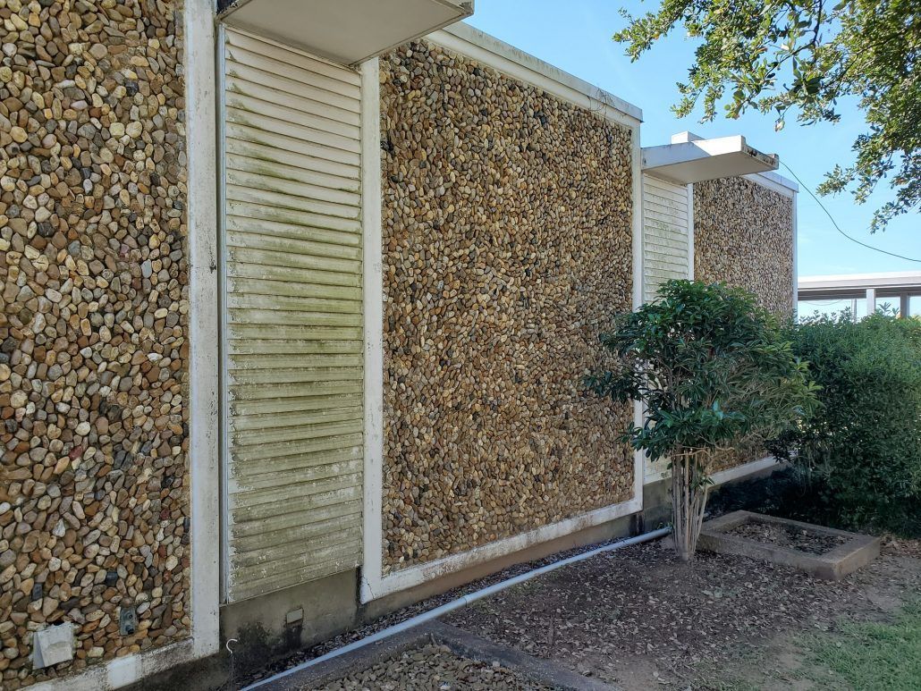 A stone wall with a window and a tree in front of it.