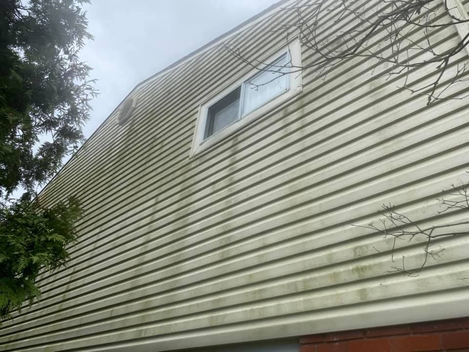 The side of a house with a window and a tree in the background.