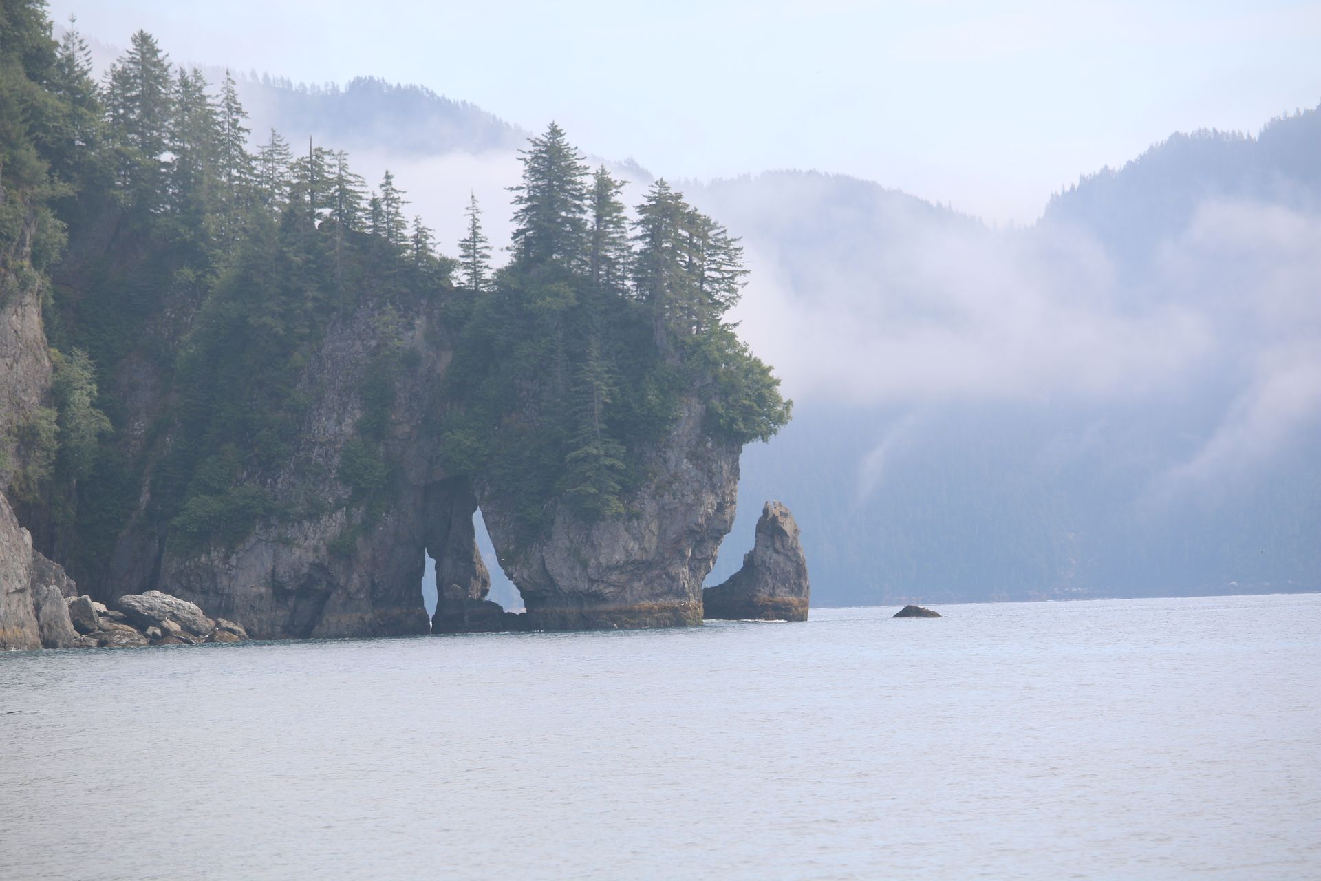 A large rock formation in the middle of a body of water with mountains in the background.