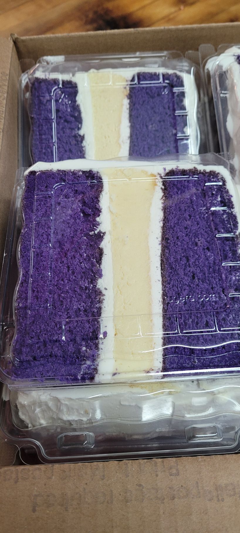 A purple and white cake is in a plastic container.