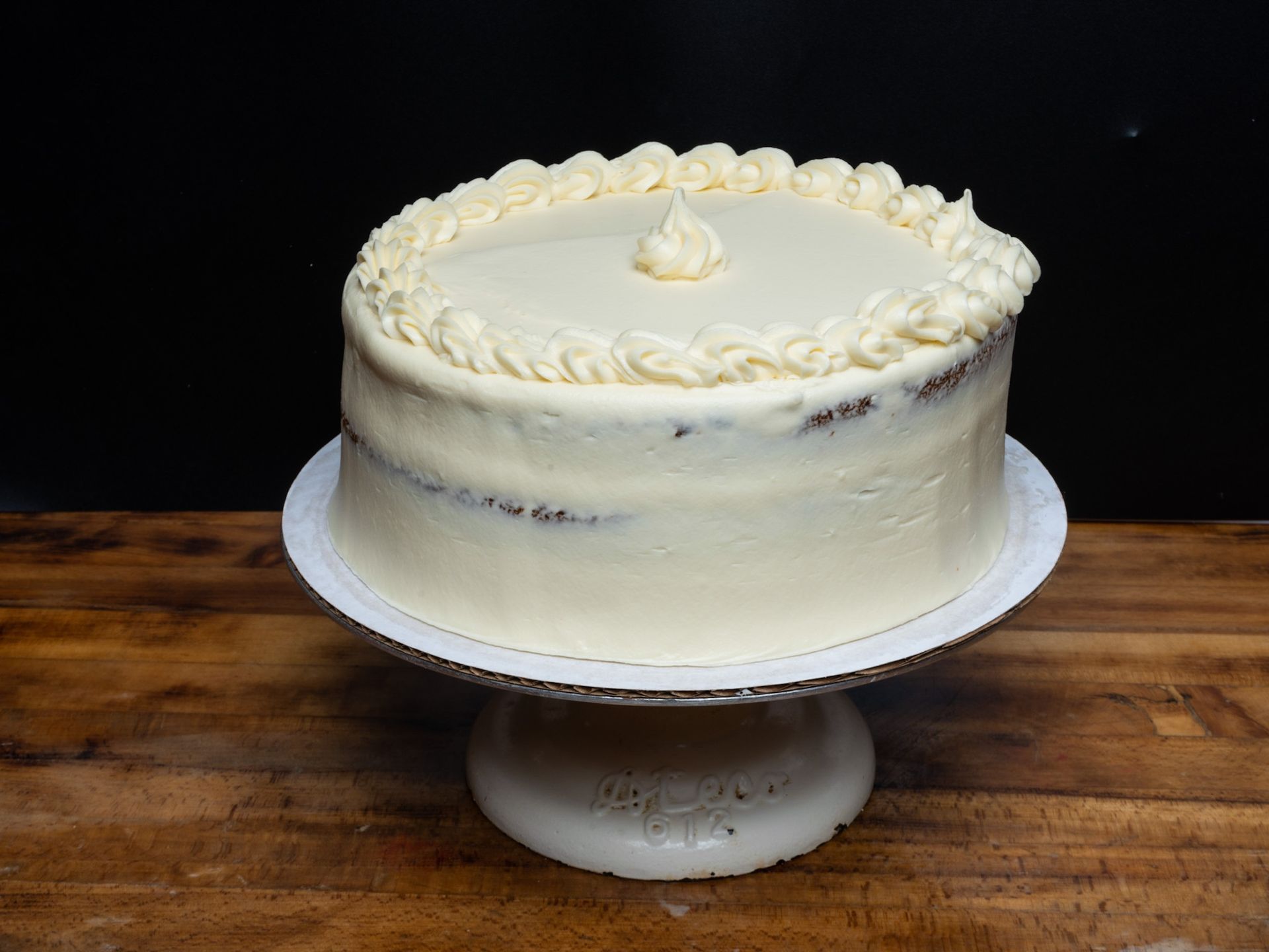 A white cake is sitting on top of a white cake stand on a wooden table.