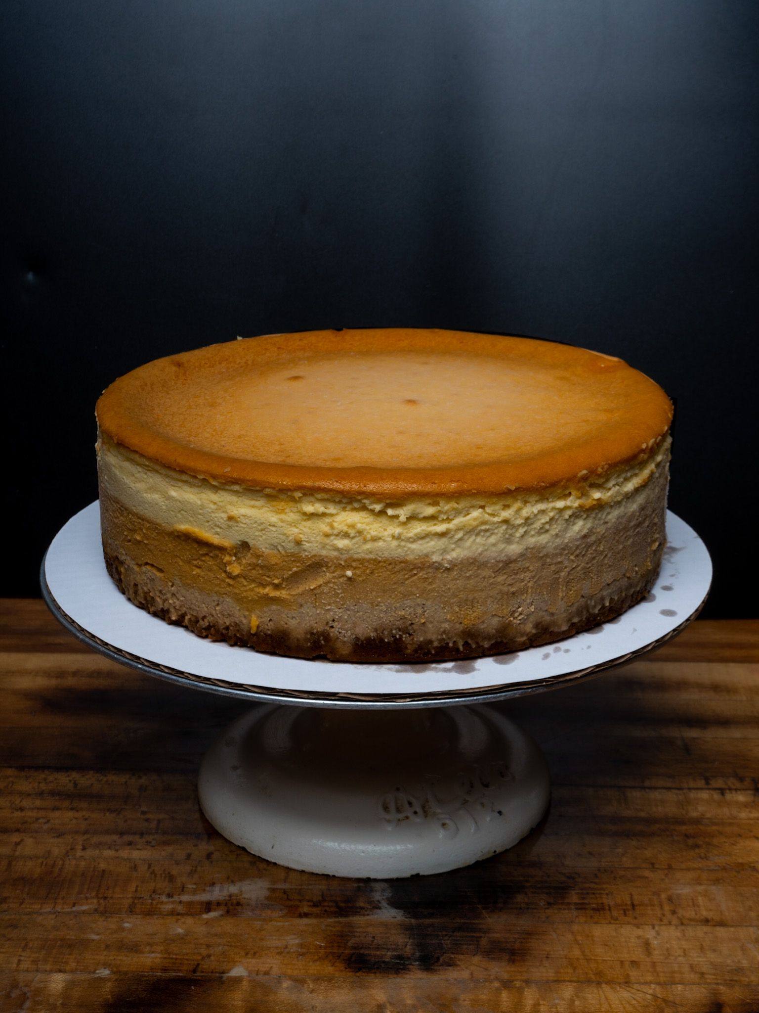 A cheesecake is sitting on top of a cake stand on a wooden table.