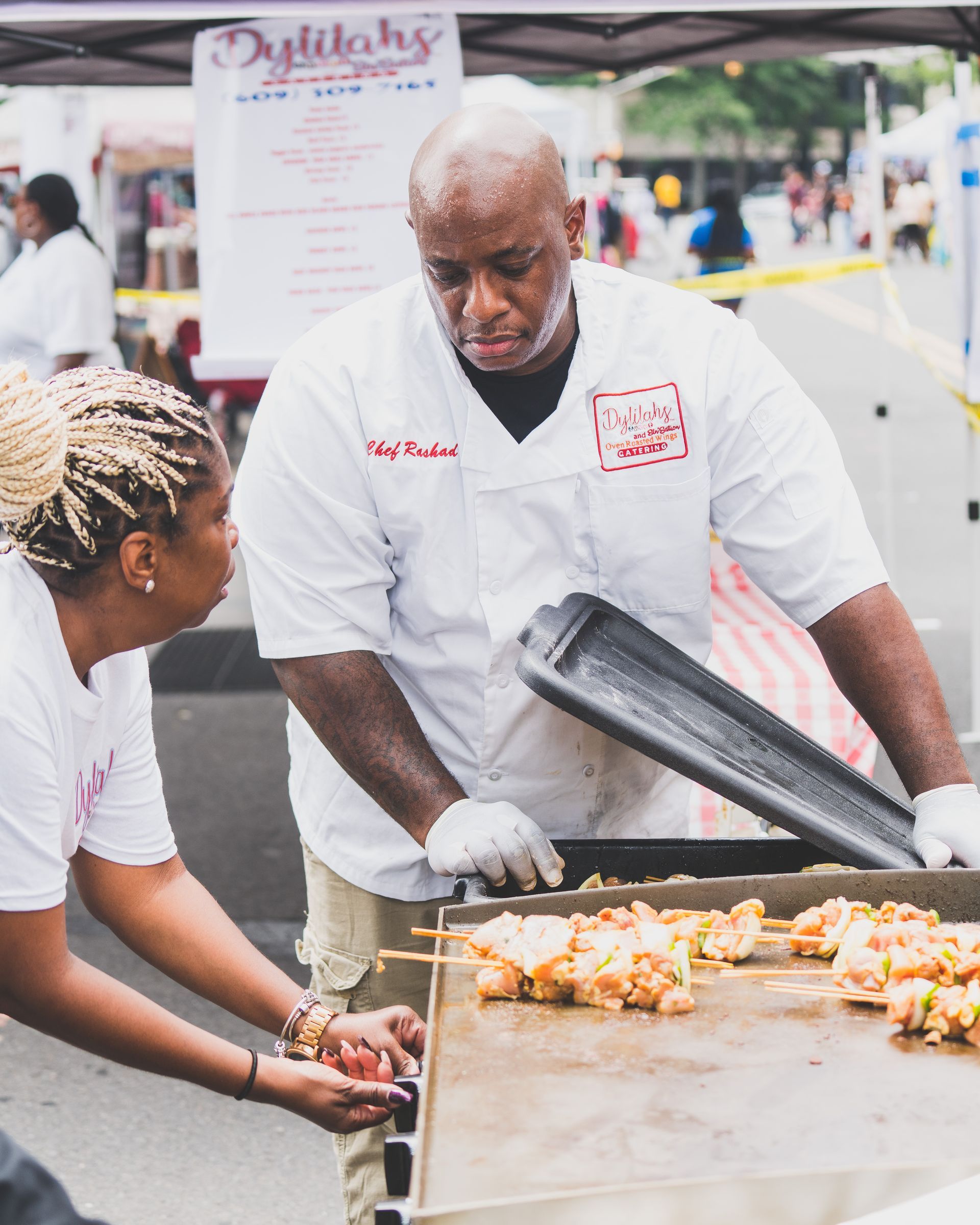 A man and a woman are preparing food on a grill.