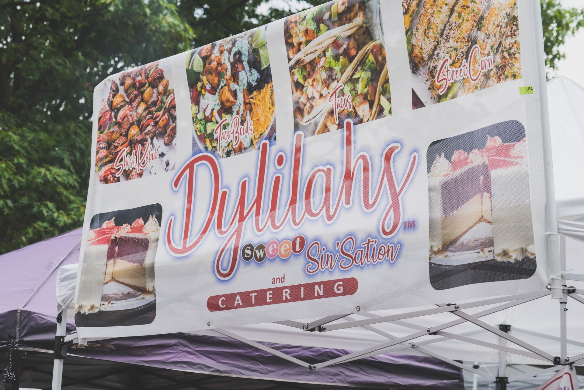 A sign for dylilah 's catering is hanging from a tent.