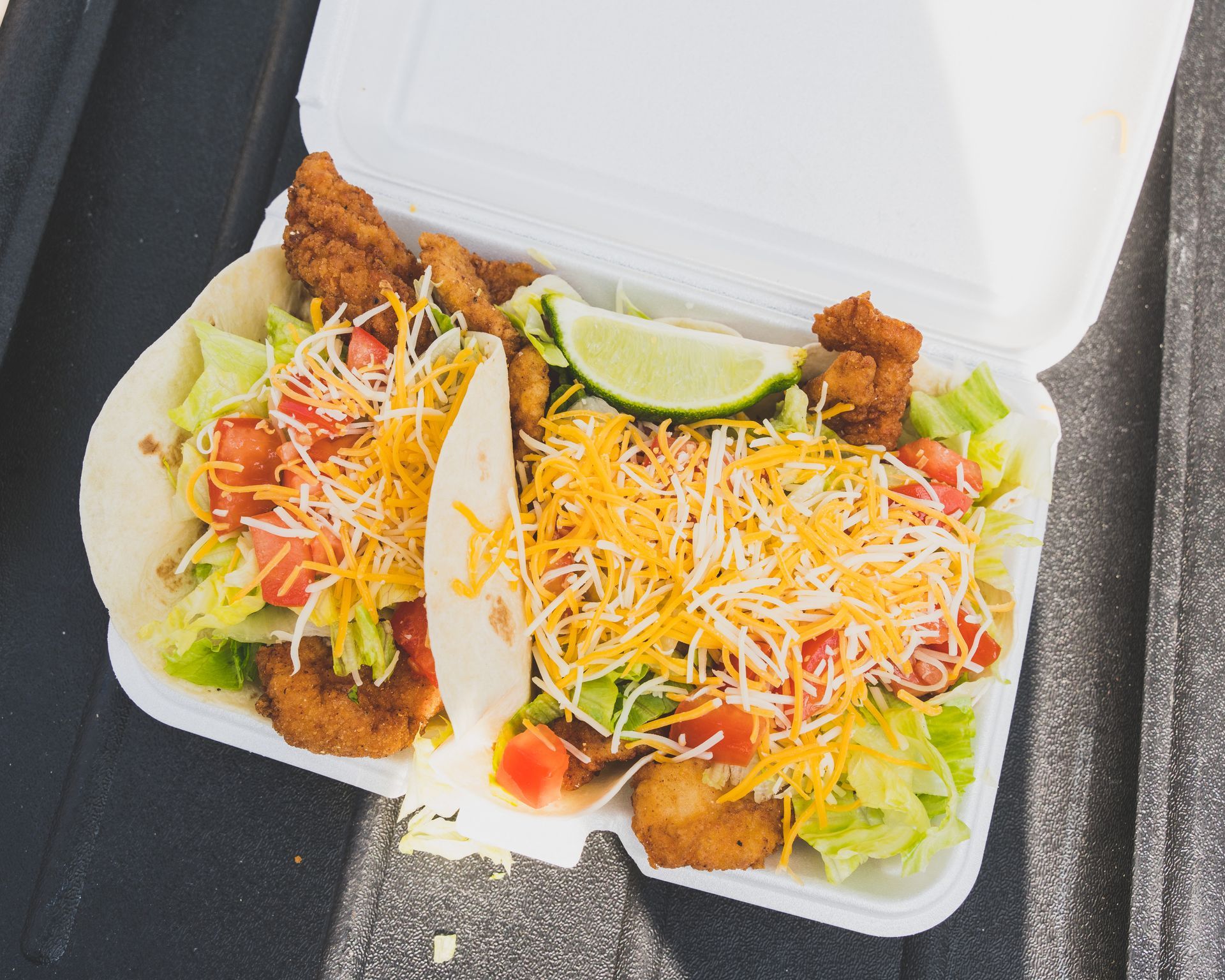 A styrofoam container filled with tacos and lettuce