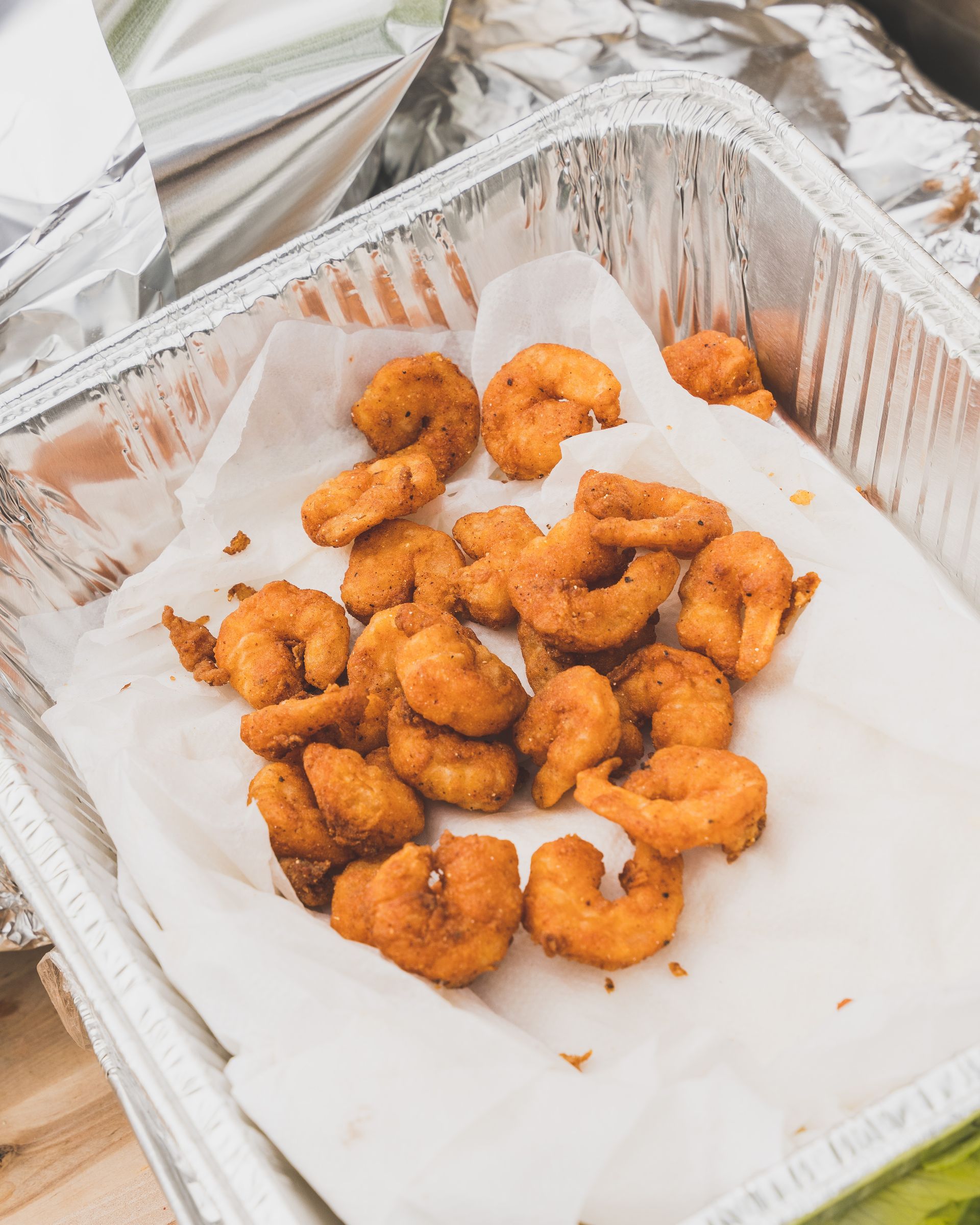 Aluminum foil container filled with fried shrimp on a paper towel.