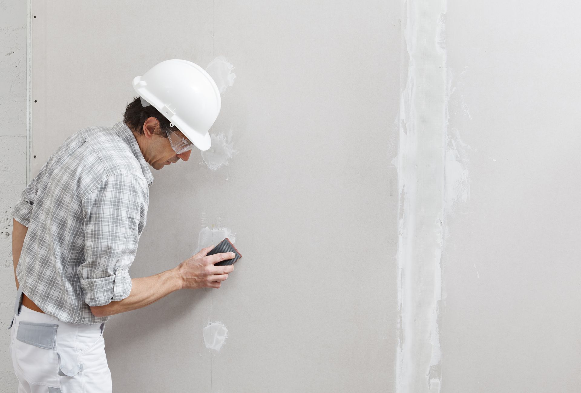 A man is sanding a wall with a sander.