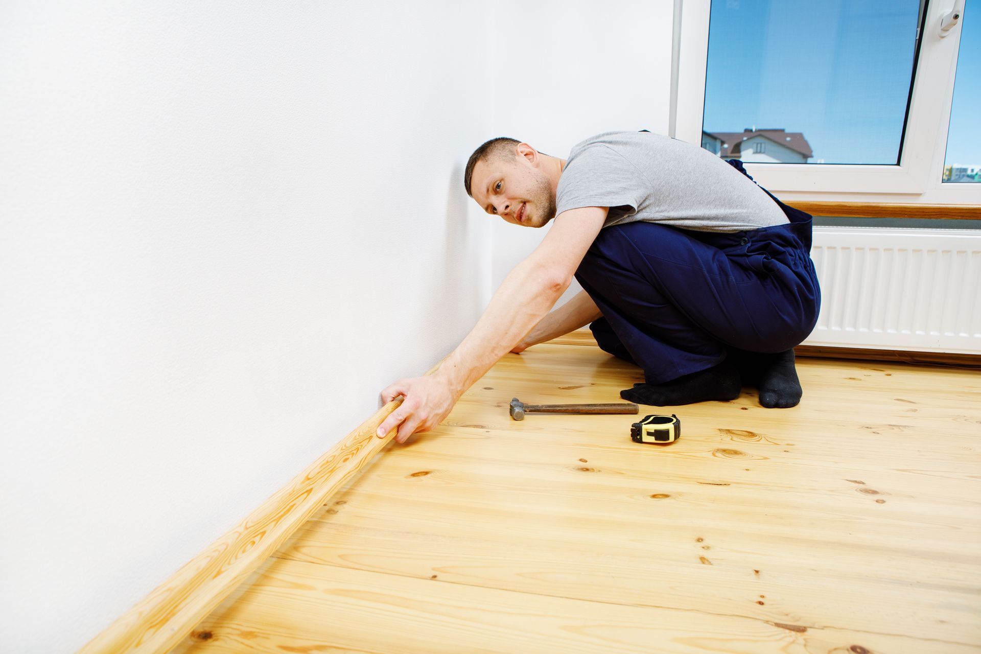 A man is kneeling on the floor while working on a wooden floor.