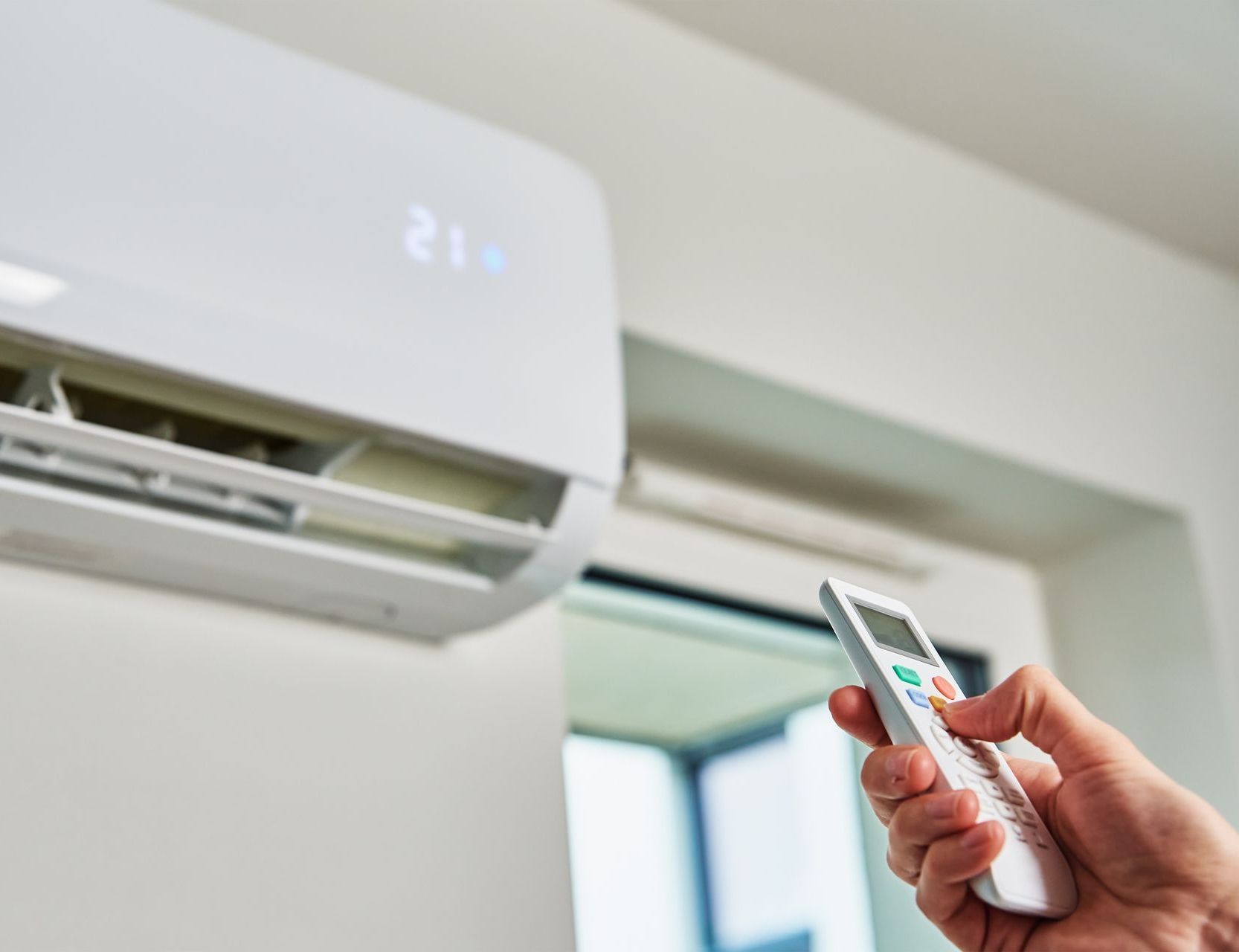 Une personne tient une télécommande devant un climatiseur.
