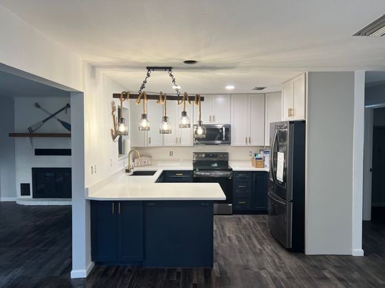 A kitchen with blue cabinets , white counter tops , stainless steel appliances and a black refrigerator.