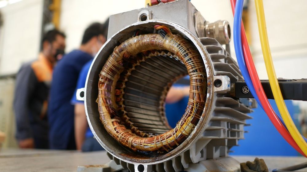Open electric motor with copper windings, viewed close-up. Men in the background— Davidson's Electrical In Parkhurst, QLD