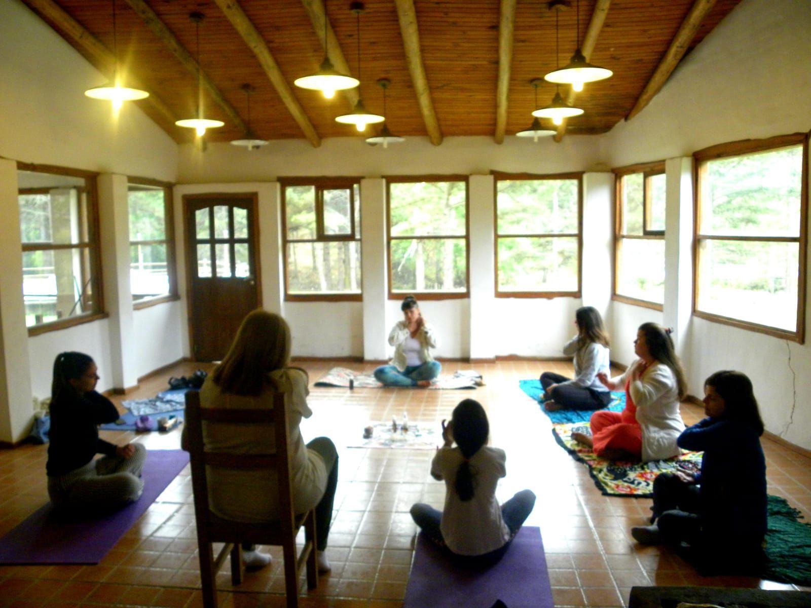 Personas en una clase de yoga, sentadas en colchonetas en una habitación luminosa con muchos ventanales.