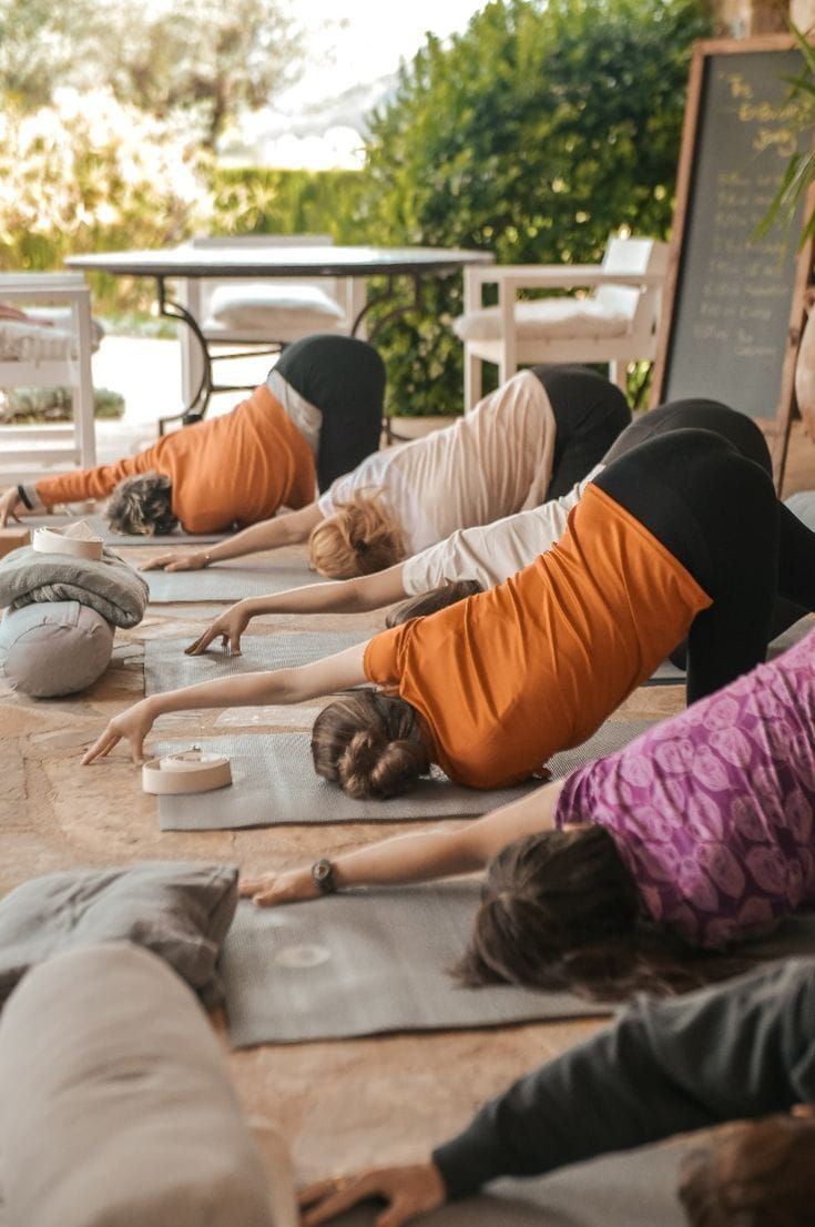 Personas practicando yoga al aire libre, estirándose hacia adelante sobre las colchonetas.