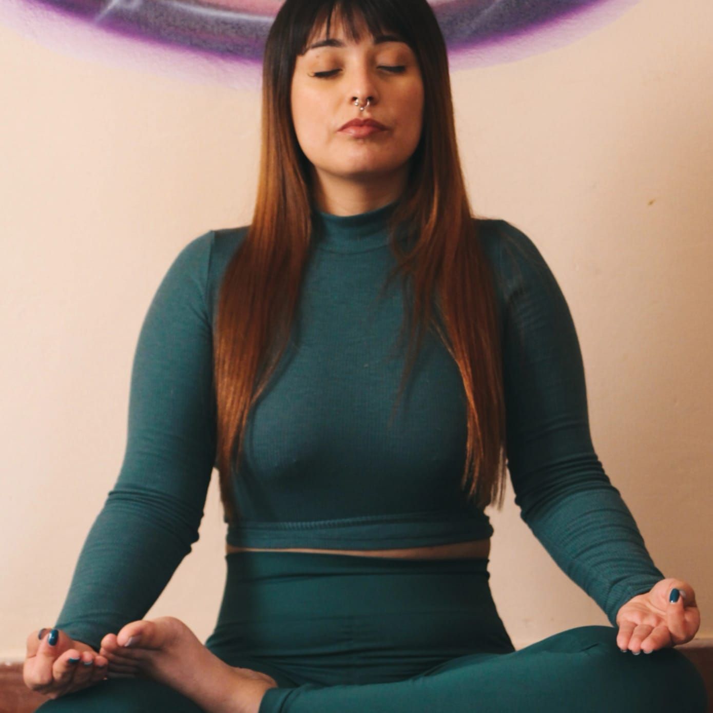 Mujer vestida de color verde azulado, meditando con los ojos cerrados en posición de loto.
