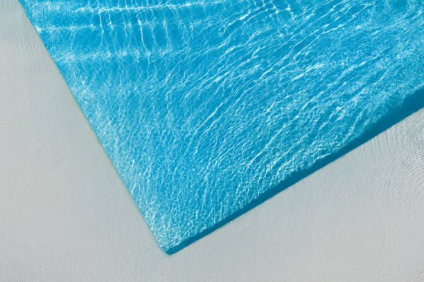 A close-up, high-angle view of a corner of a bright blue swimming pool with rippling water against a light grey deck.