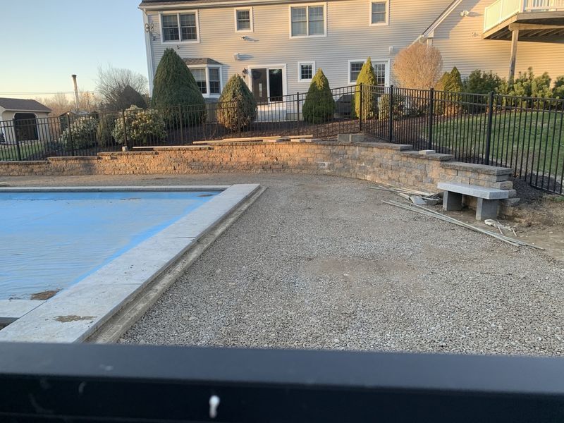 A residential backyard featuring a covered swimming pool, a gravel patio, and a stone retaining wall against a two-story house.