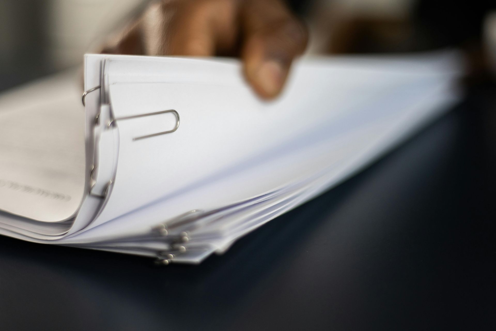 Hand turning a metal paper clip on a stack of white papers in a binder