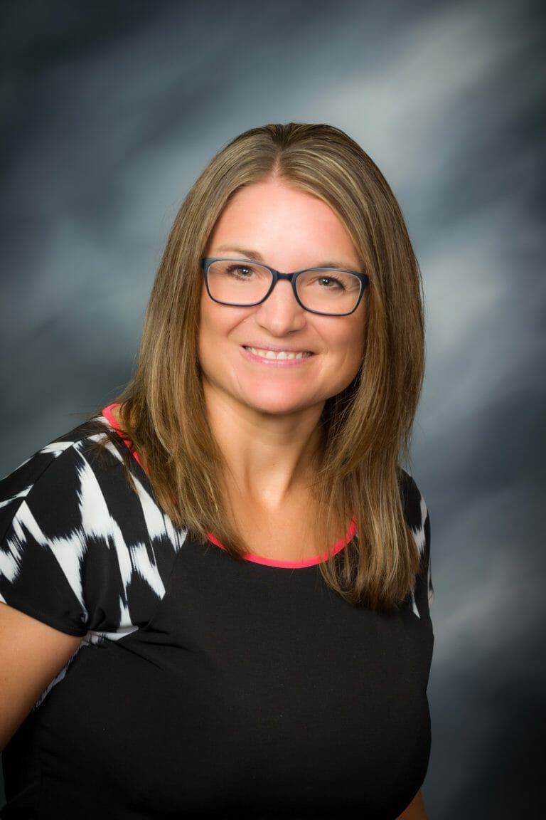 A woman wearing glasses and a black shirt is smiling for the camera.