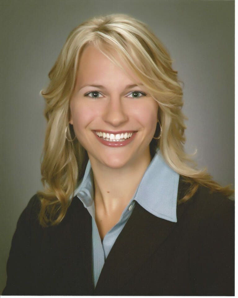 A woman in a suit and blue shirt is smiling for the camera