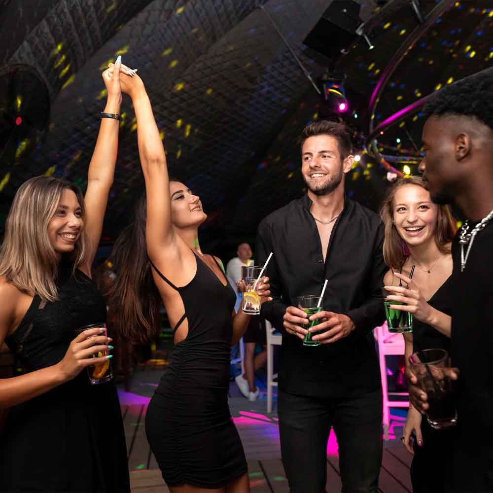 Five friends dancing and drinking cocktails in a club with colorful lights; all wearing black clothing.