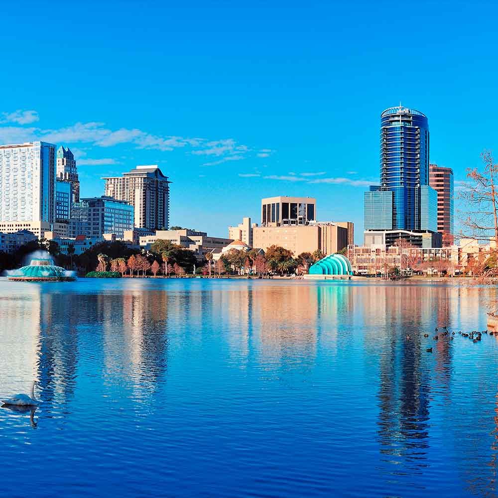 Orlando, Florida skyline reflected in blue lake under a clear, sunny sky.