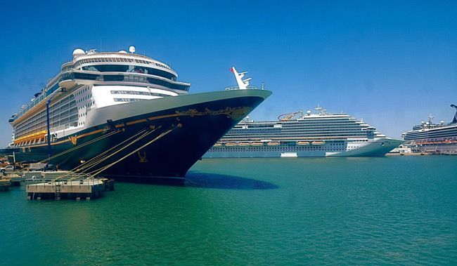 Several cruise ships docked in a harbor, against a bright blue sky.