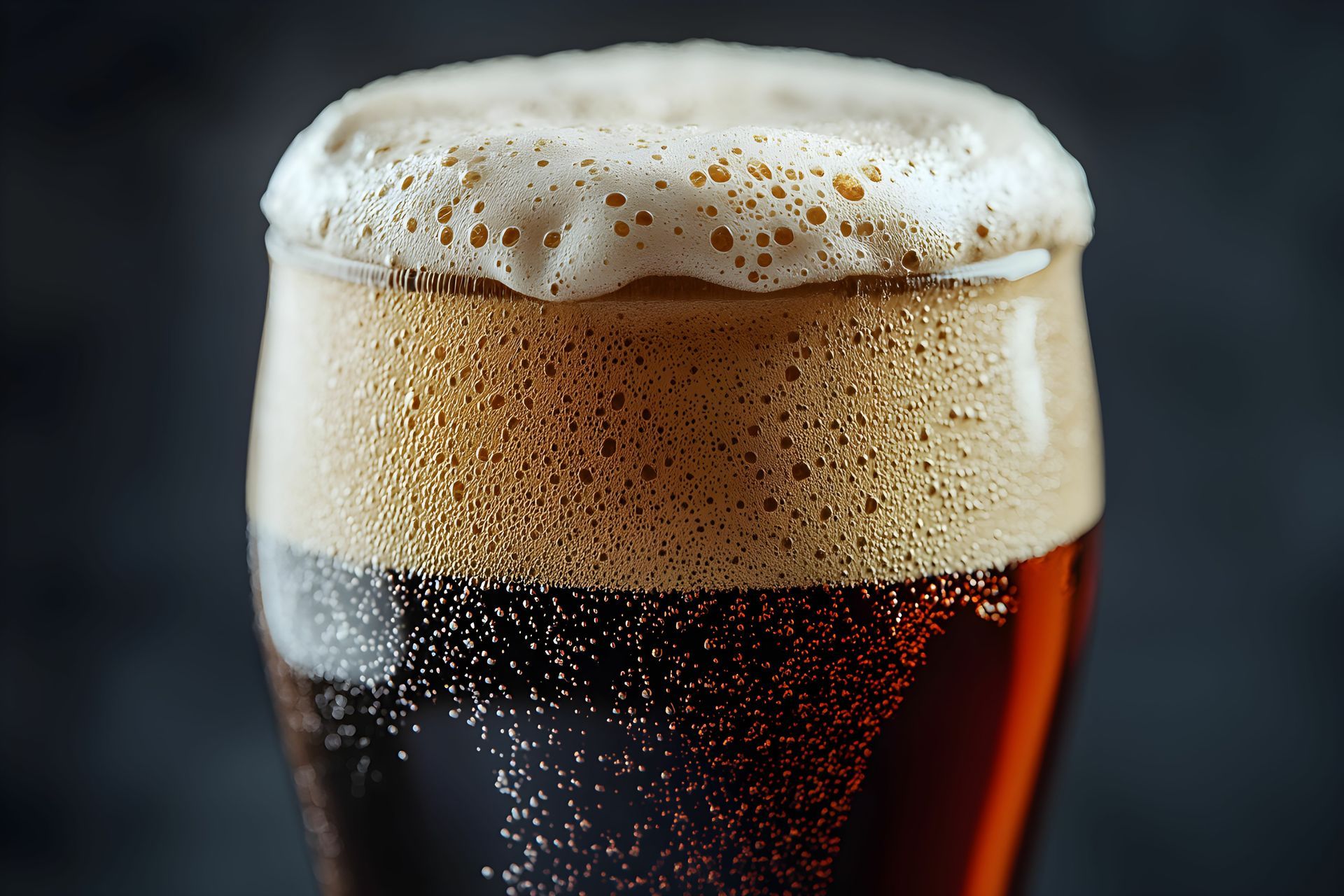 A close up of a glass of beer with foam on top.