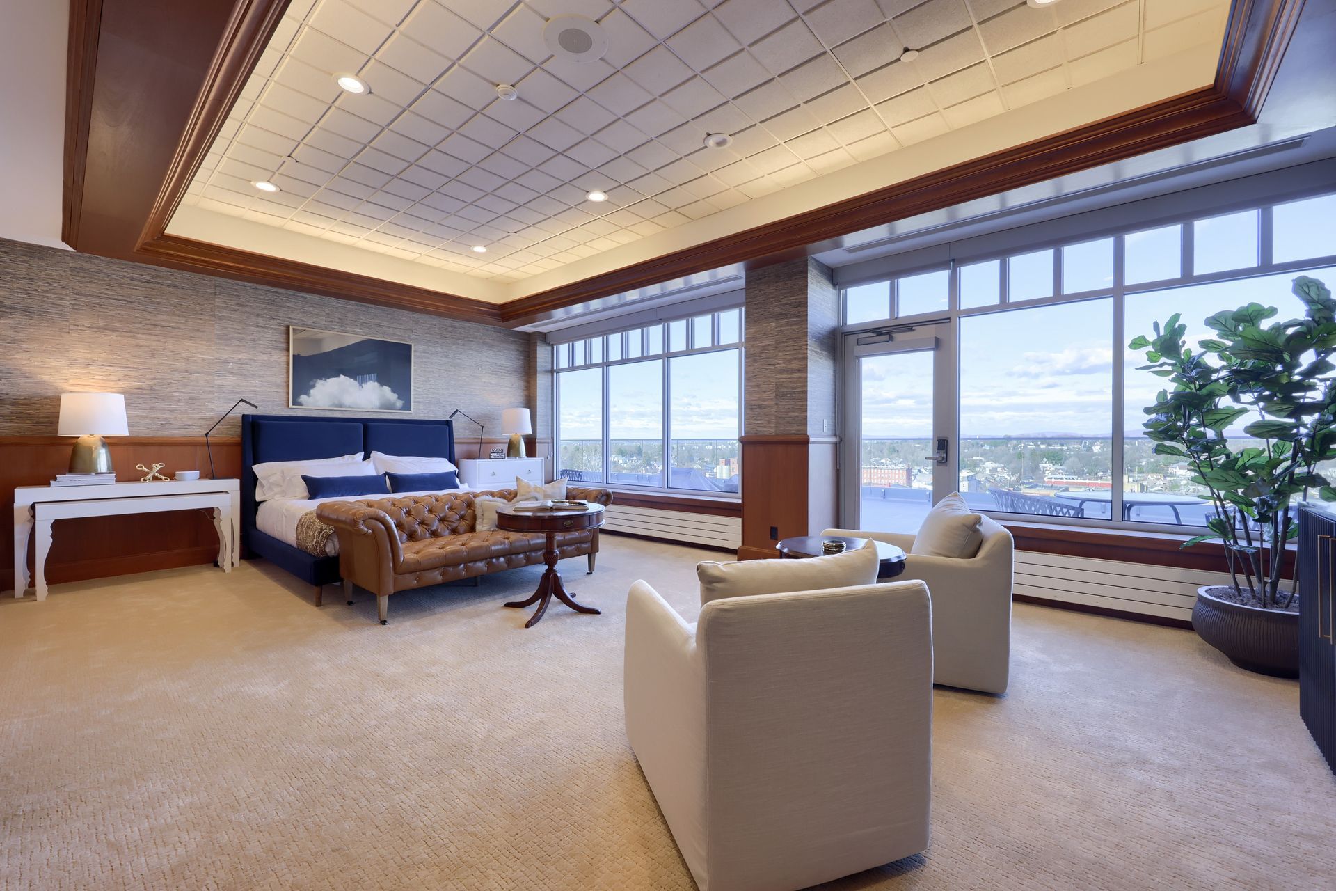 A hotel room with a large bed , couch , chairs and lots of windows