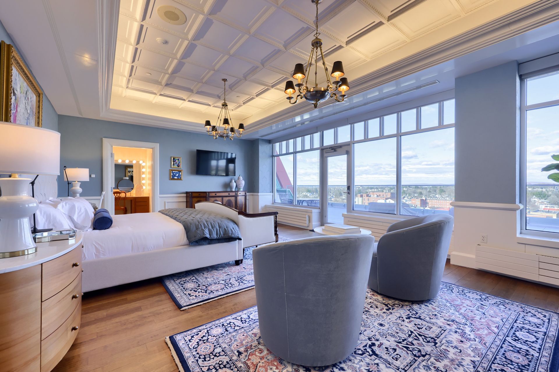 A large bedroom with a king size bed , two chairs , a rug and a chandelier.