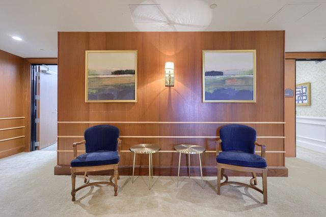 A waiting room with two chairs and two tables and two paintings on the wall.