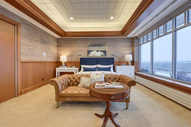 A bedroom with a large bed , couch , table and windows.