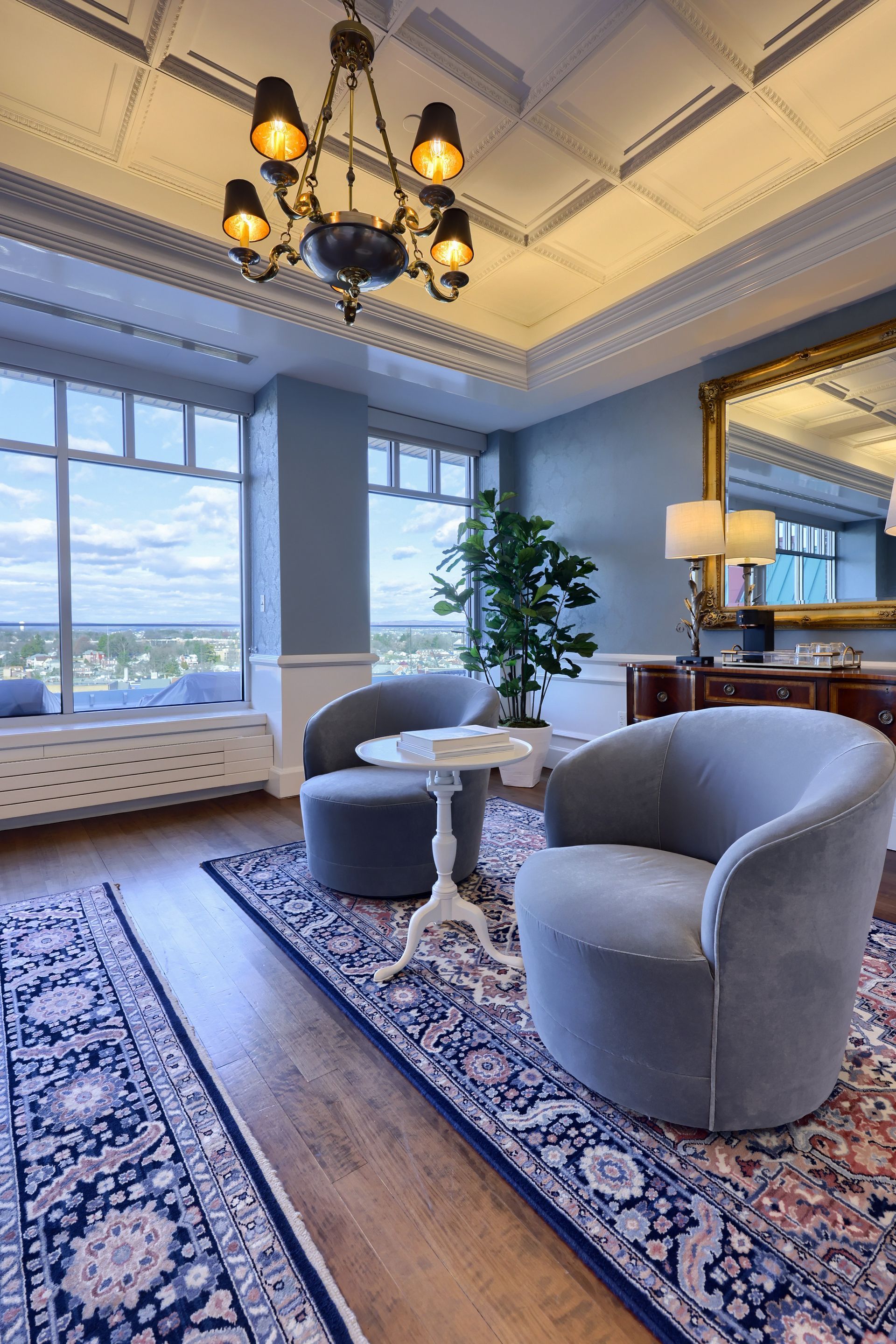 A living room with two chairs , a table , a mirror and a chandelier.