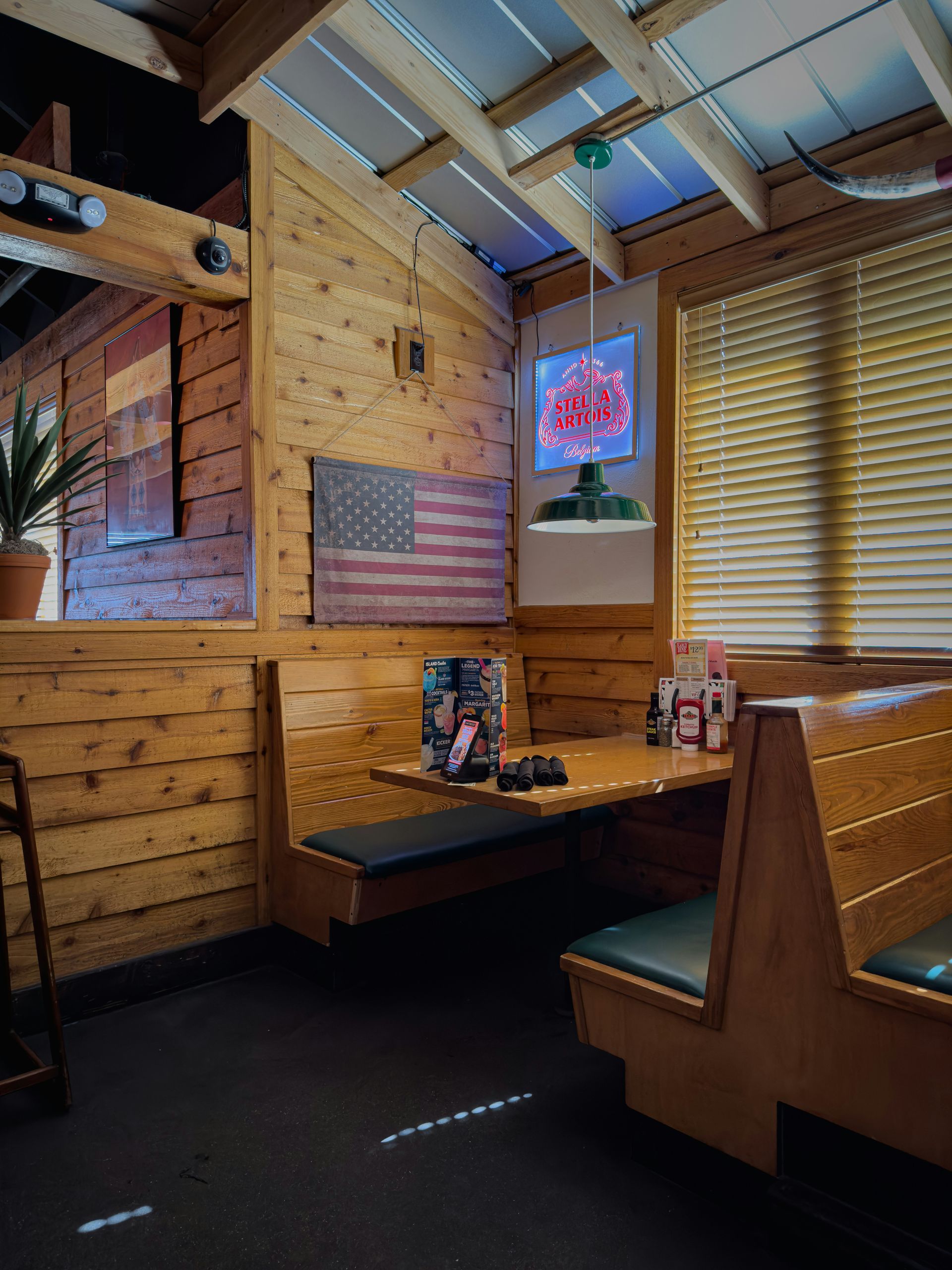 Booth seating area in a restaurant with wood paneling, an American flag, and a TV screen.