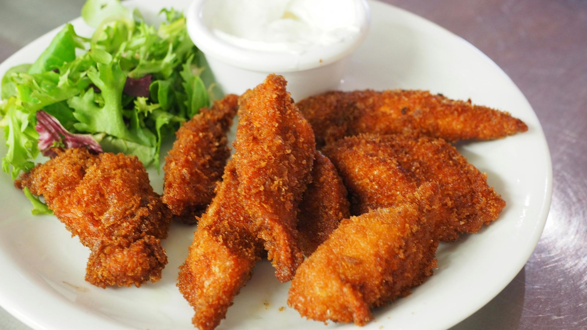 Fried chicken tenders with dip and salad on a white plate.
