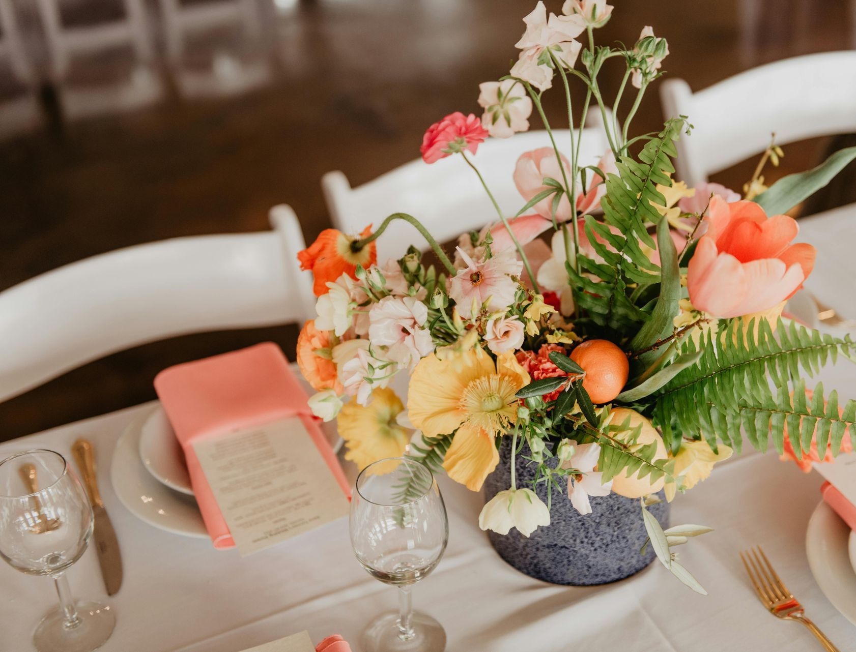Floral centerpiece on a table set for a wedding, with pink and yellow flowers, white plates, and a pink menu.