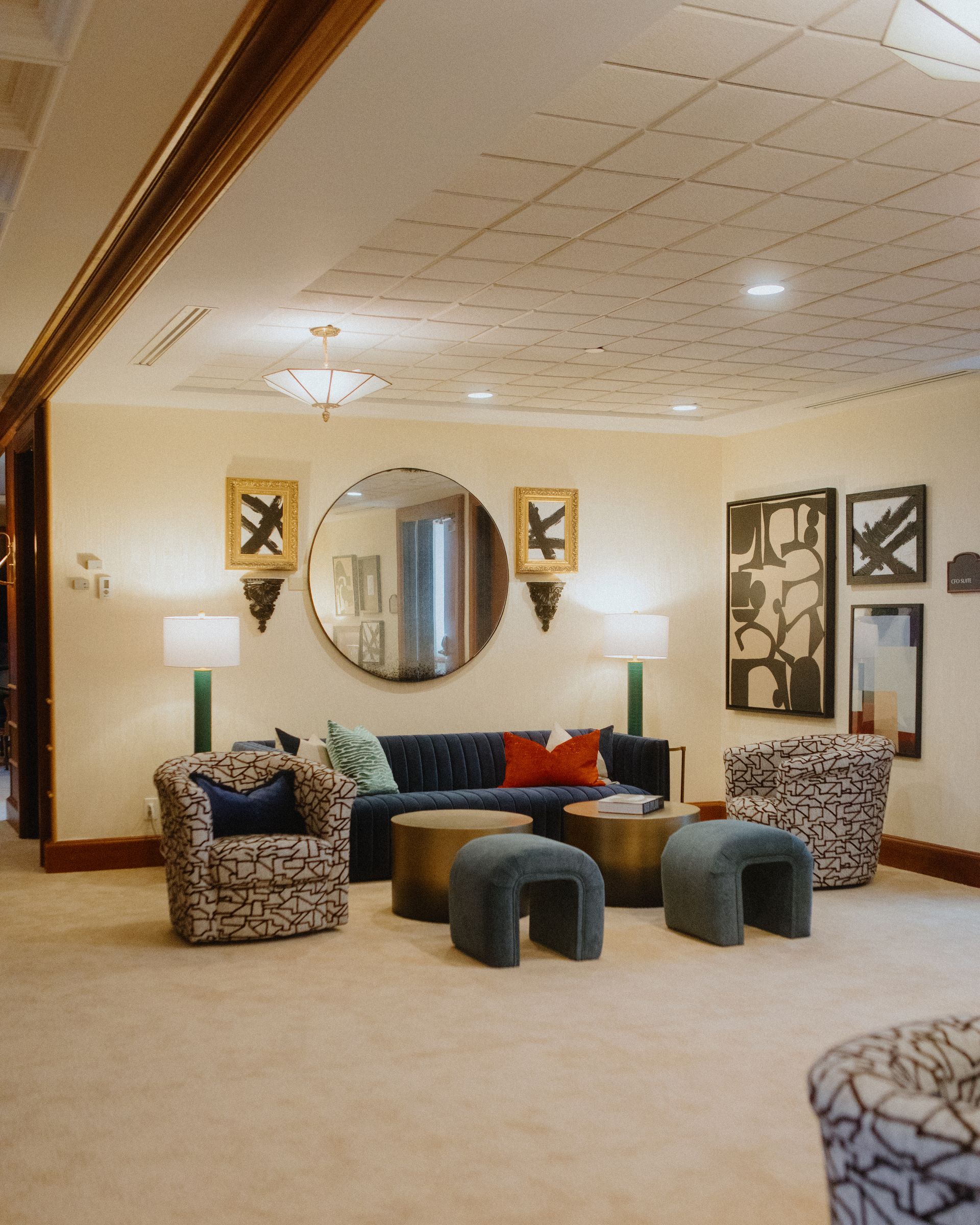 Lounge area with a blue sofa, patterned armchairs, art, and teal stools. Neutral walls and ceiling.
