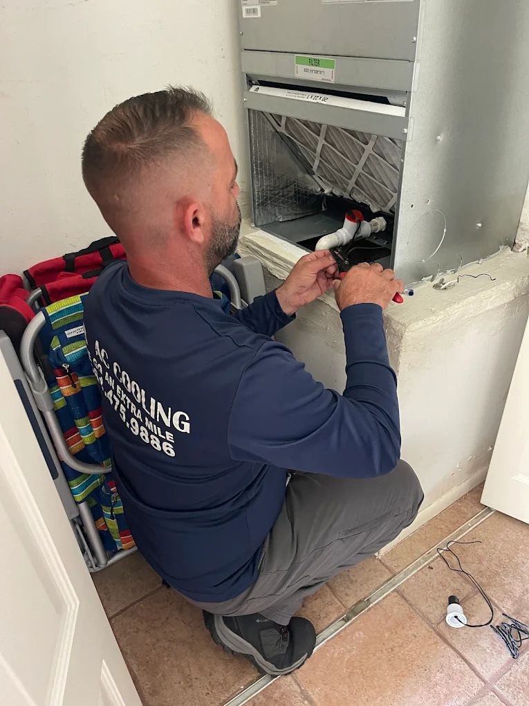 Man in blue shirt works on an HVAC unit, crouching near a white base in a tiled room.
