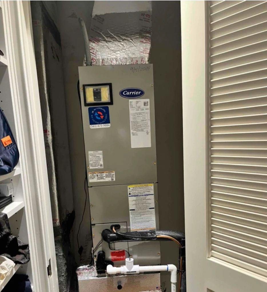 A Carrier HVAC unit installed in a closet. Silver ductwork connects to the top. White piping is visible below.