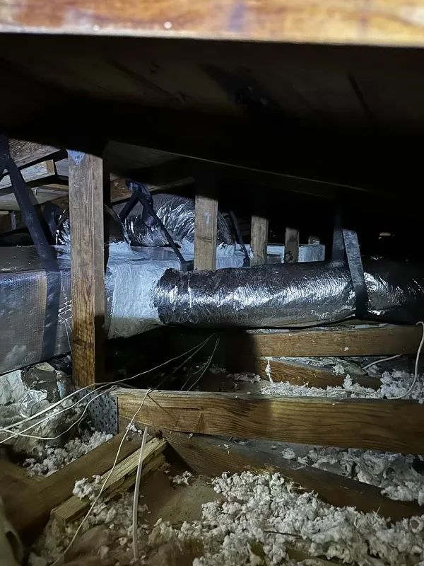 Interior view of an attic, showing ductwork, insulation, and wooden supports.