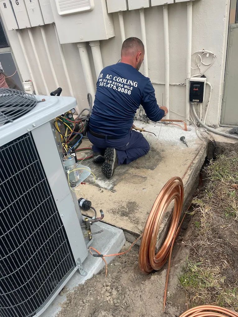 HVAC technician in blue shirt installing copper tubing near AC unit.