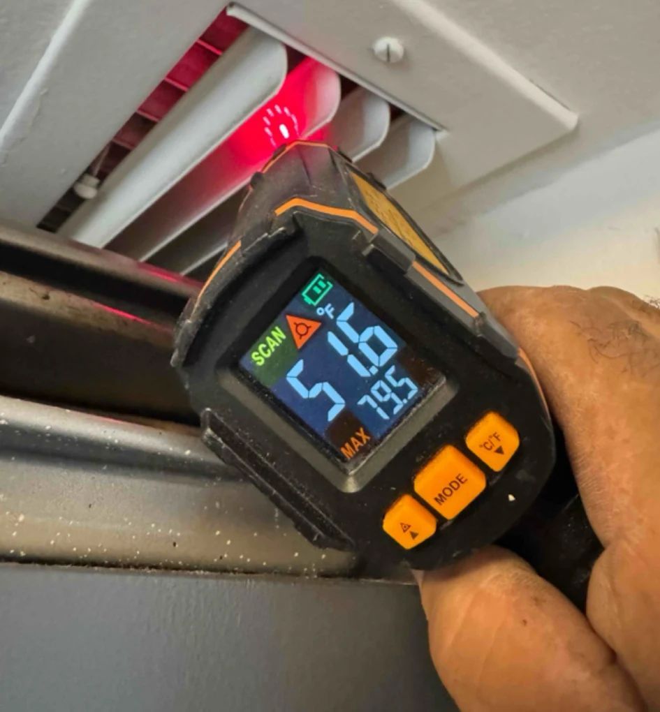 Hand using a digital thermometer to measure temperature inside an air vent. The thermometer reads 51.6 and 79.5.