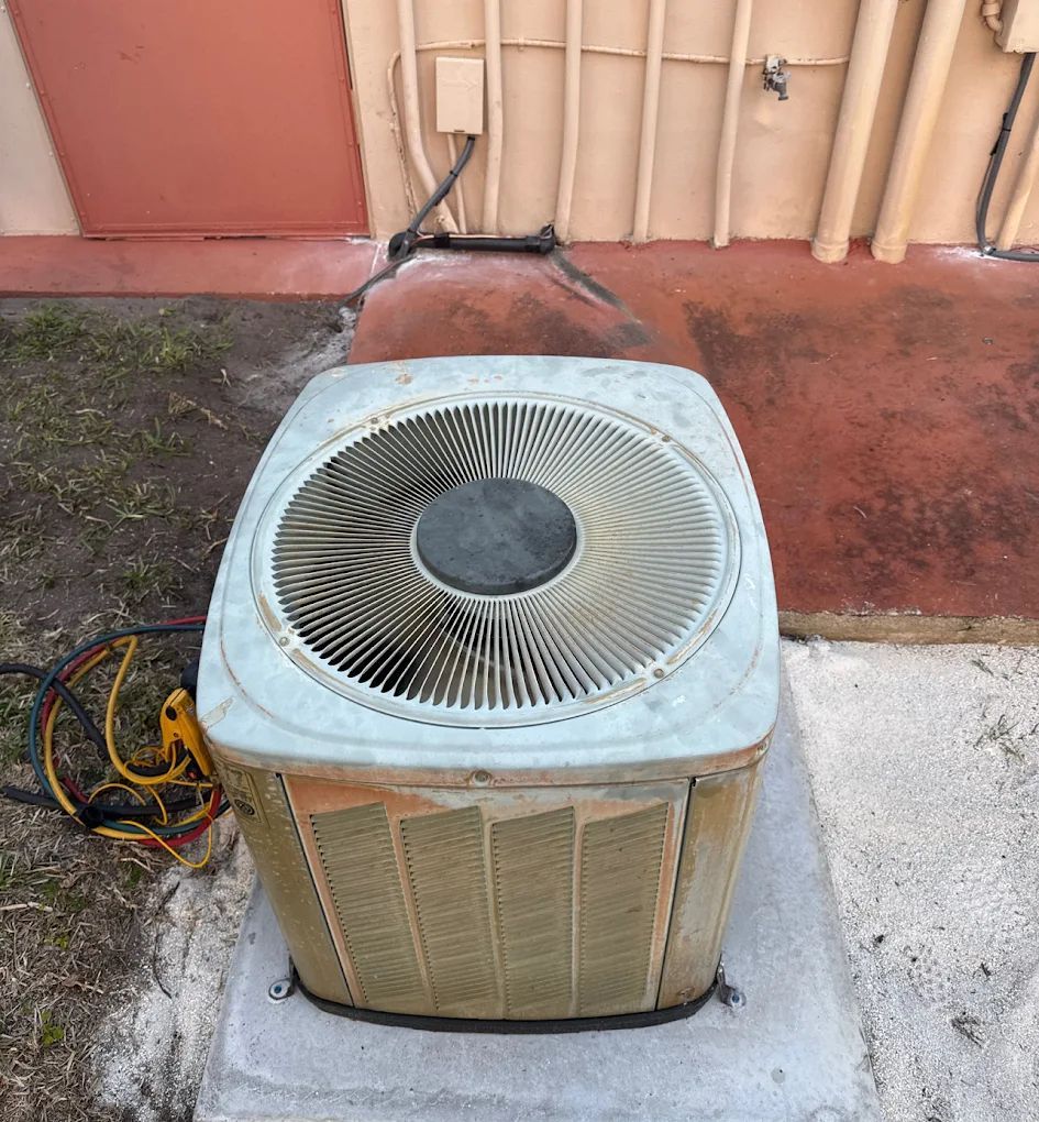 An old air conditioning unit, outside on a concrete pad, against a wall.