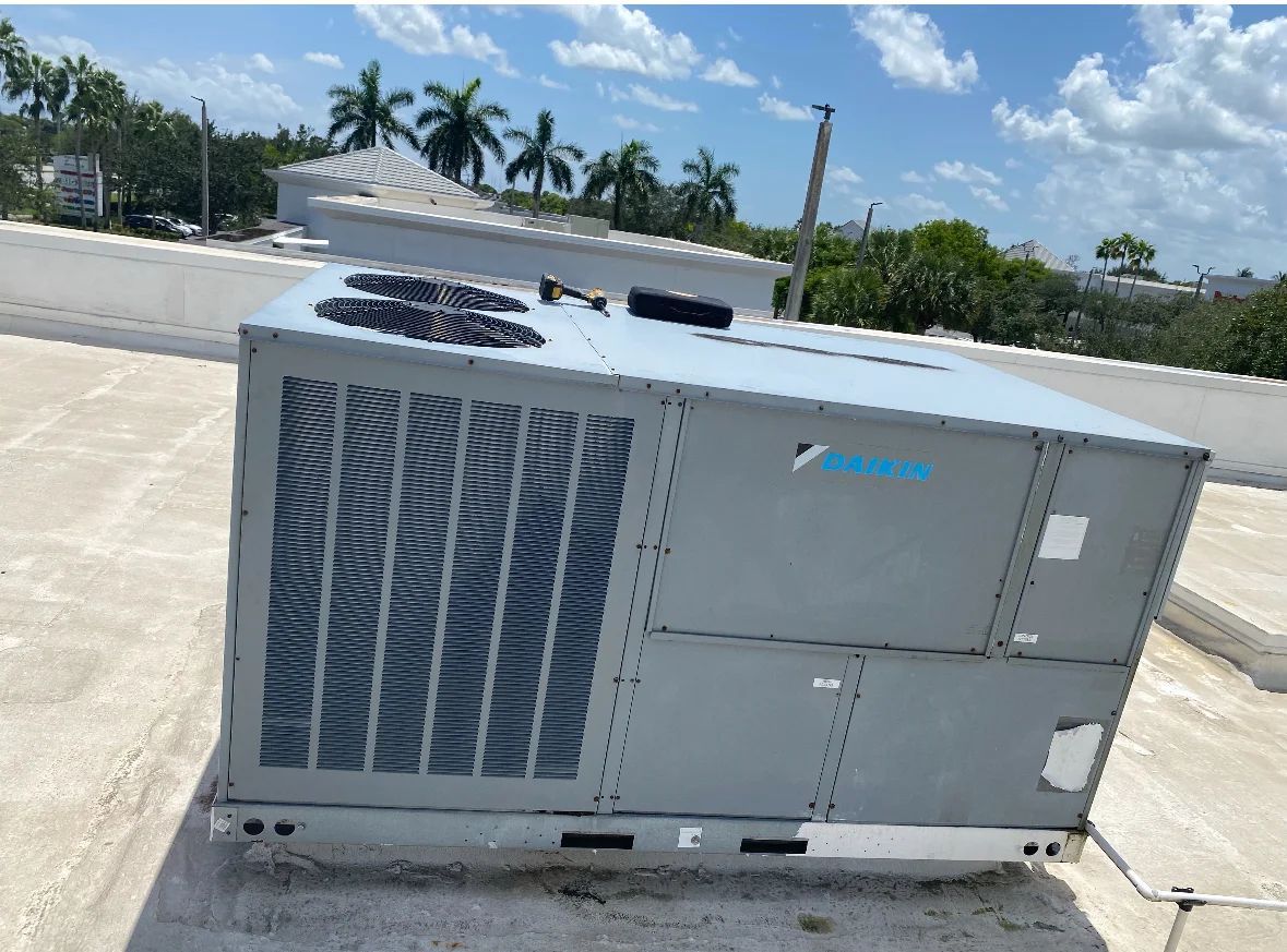 Rooftop Daikin HVAC unit; gray metal box with fan, vents, and blue logo against a blue sky.