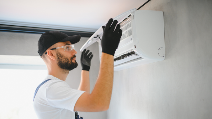 Man in black gloves and cap fixing a wall-mounted air conditioner.