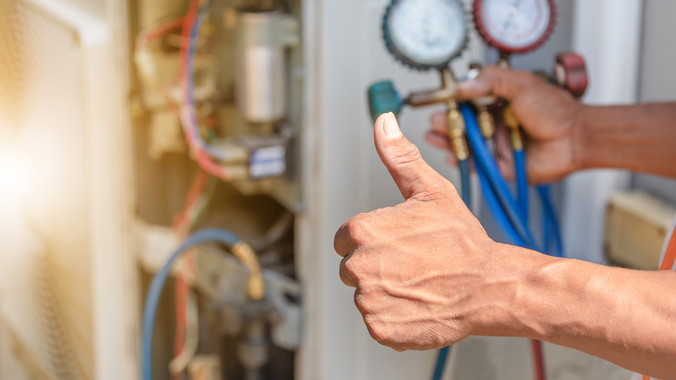 HVAC technician giving thumbs up while working on air conditioning unit.