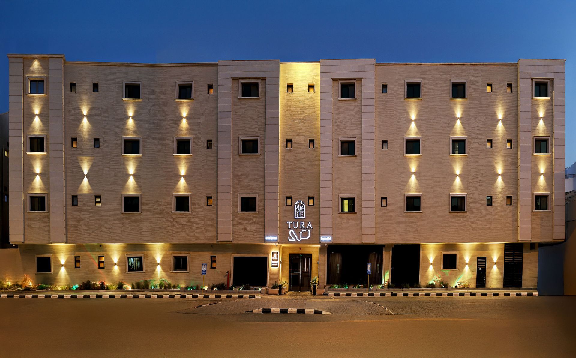 A multi-story hotel building with stone-textured walls, illuminated by warm exterior sconce lighting at dusk.