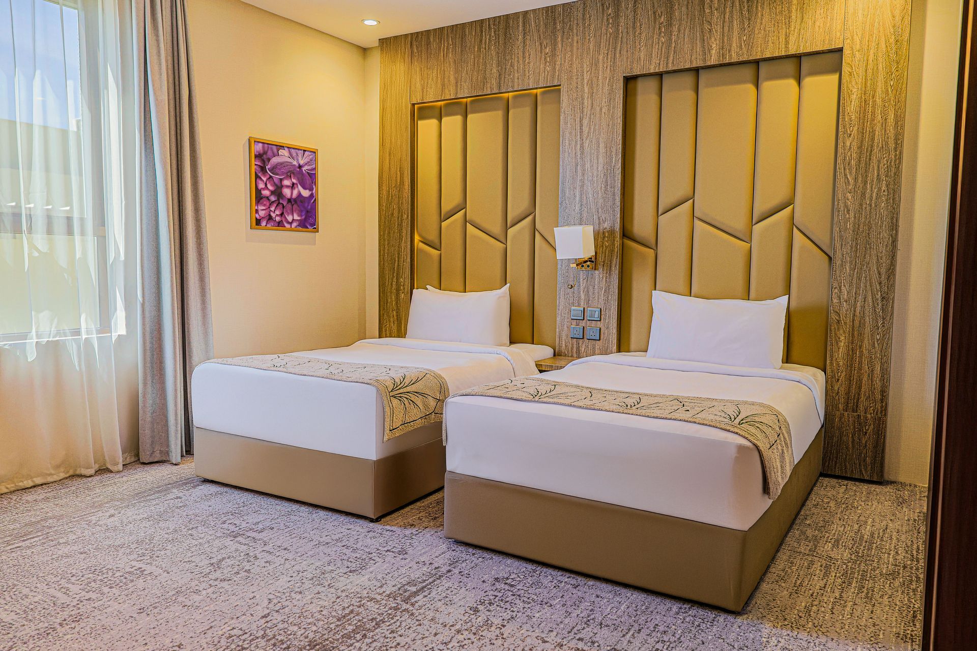 A hotel room featuring two twin beds with white linens, tan patterned headboards, and light patterned carpet.